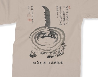 Puede incluir: Una camiseta beige con una ilustración en blanco y negro de un gato. El gato está dibujado en estilo japonés con un círculo alrededor de su cuerpo. El texto en la camiseta dice: "中林行五人很直立的重叼仑瓦丹比林因饥尤".