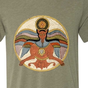 Puede incluir: Una camiseta verde con un gráfico circular de una criatura alada roja con un diamante en el pecho. La criatura está rodeada de un círculo dorado con un halo multicolor.