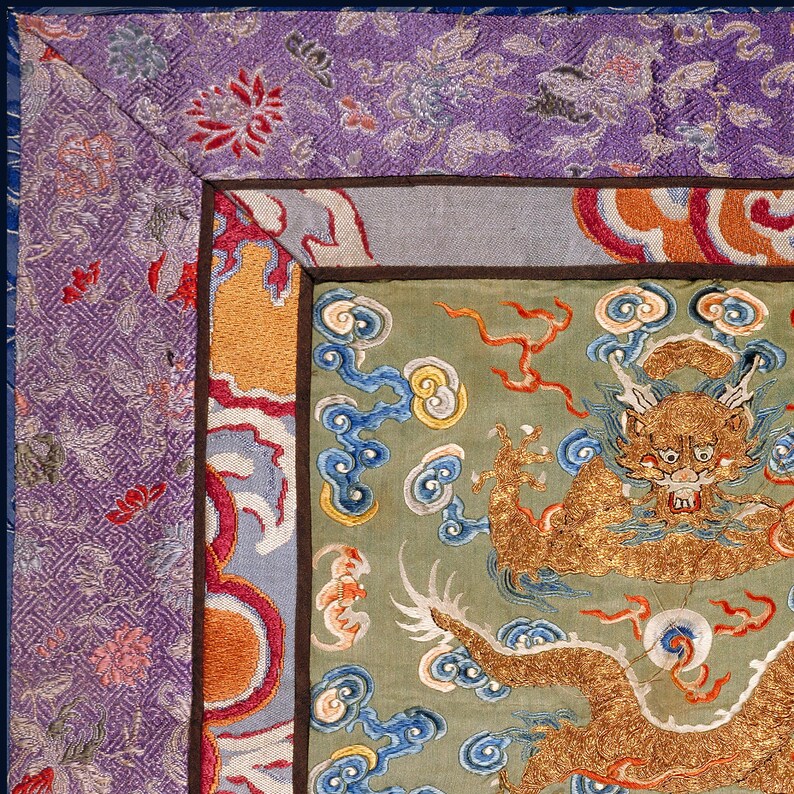 Pode incluir: Close-up de um drag&atilde;o bordado a ouro sobre um fundo verde. O drag&atilde;o &eacute; rodeado por nuvens azuis e amarelas. A borda do tecido &eacute; um padr&atilde;o roxo e azul.