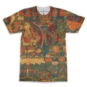 May include: A short-sleeved t-shirt with a vibrant, detailed illustration of two figures in a traditional style. The artwork features red, orange, green, and blue hues, with intricate patterns and figures. The shirt has the text "SACRED SURREAL" on the collar.