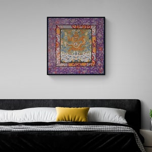 Pode incluir: Uma obra de arte emoldurada apresentando um design bordado colorido de um drag&atilde;o em um mar de ondas. O drag&atilde;o &eacute; dourado e vermelho, e as ondas s&atilde;o azuis e brancas. A moldura &eacute; preta e a obra de arte &eacute; cercada por uma borda roxa com padr&otilde;es florais.
