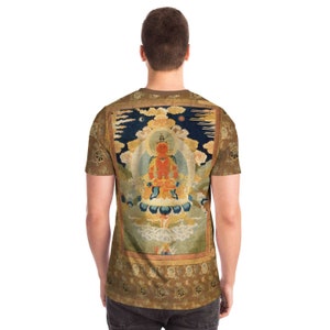 May include: A brown t-shirt featuring a detailed illustration of a seated figure with a halo, set against a backdrop of clouds and a night sky. The shirt has a repeating floral pattern on the sleeves and the body.