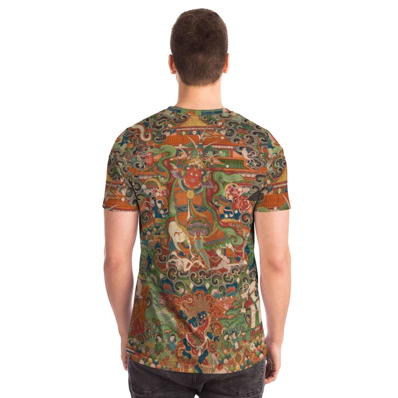 May include: A short-sleeved t-shirt featuring a detailed, colorful illustration. The artwork depicts a complex scene with figures, buildings, and intricate patterns in shades of red, green, orange, and blue. The shirt's design covers the entire surface.