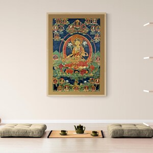 May include: A colorful Tibetan Buddhist thangka painting depicting a deity in a seated position surrounded by smaller figures. The painting is framed in a gold-colored frame.