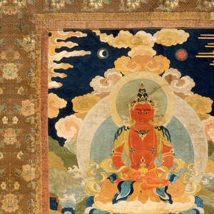 May include: A detailed, colorful tapestry depicting a seated figure with a red complexion, adorned with gold jewelry and a crown. The figure is surrounded by clouds, a crescent moon, and a sun against a dark blue background. The tapestry has a decorative border.