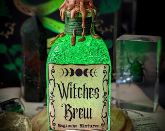 Puede incluir: Una pequeña botella de vidrio con un líquido verde, sellada con cera marrón. La etiqueta dice "Witches Brew Magische Mixturen".