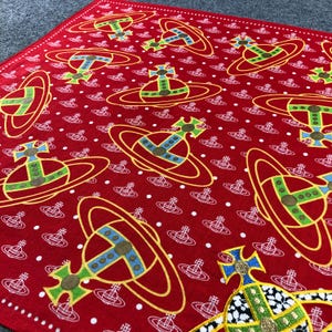 Könnte beinhalten: Roter Stoff mit einem sich wiederholenden Muster eines planetenähnlichen Designs in Gelb, Grün, Blau und Weiß. Der Stoff hat auch kleine weiße Punkte und ein sich wiederholendes weißes Logo. Das Design ist ein auffälliges Muster.
