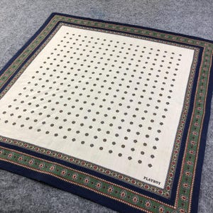May include: A white bandana with a navy blue, green, and red border. The bandana has a repeating pattern of small white flowers on a white background. The text "PLAYBOY" is printed in the bottom right corner.