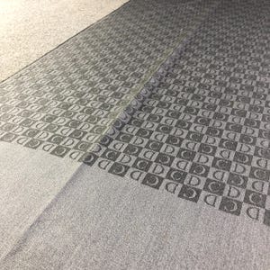 May include: A close-up of a gray fabric with a repeating pattern of black letters. The letters are arranged in a checkered pattern.