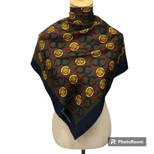 May include: A green, red, and blue silk scarf with a chain link pattern and gold medallions. The scarf is folded and displayed on a mannequin. The text "Annalaura" is printed on the scarf.