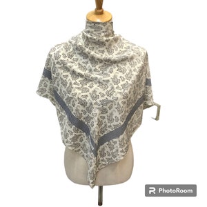 Puede incluir: Un pañuelo de seda blanco con un patrón de paisley en negro y azul. El pañuelo tiene un borde a cuadros blanco y negro.