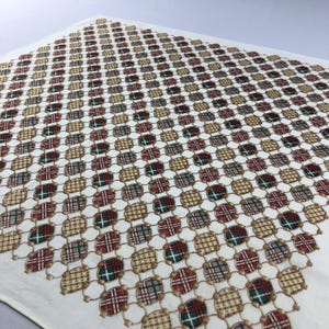 May include: A square textile featuring a repeating pattern of oval shapes connected by thin gold-coloured chain links. Each oval contains a plaid design in alternating colours of red, green, and tan against a solid off-white background.