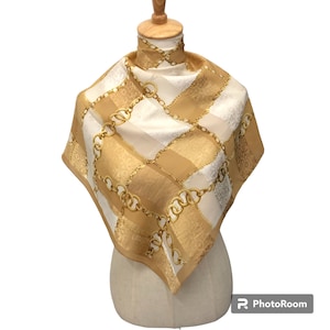 May include: A white and gold silk scarf with a chain link pattern. The scarf is displayed on a mannequin.