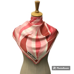 Puede incluir: Un pañuelo cuadrado de seda con un diseño abstracto en tonos rojos, rosas y blancos. El pañuelo está drapeado sobre un maniquí, mostrando su vibrante paleta de colores y patrón. El texto "DESSINS CHARLET" está impreso.