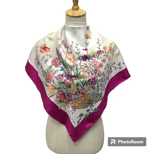 May include: A white silk scarf with a pink border features a floral print of a basket overflowing with colorful flowers. The scarf is printed with the text "FENDI ROMA".