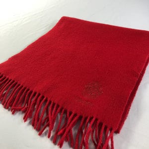 May include: A vibrant red scarf with a fringed edge. The scarf features a textured surface and a subtle embroidered design with the word "LUCKY". This accessory is suitable for adding a pop of color to any outfit.