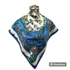 May include: A blue and white silk scarf with a colorful pattern of people and trees. The scarf is folded in a triangular shape and is displayed on a white background.