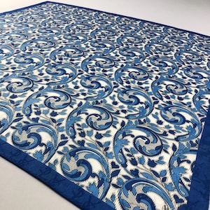 Puede incluir: Un textil cuadrado con un patrón repetitivo de diseños florales arremolinados azules y blancos. El borde es azul oscuro liso. El patrón incluye acentos azul claro y gris, creando una apariencia detallada y elegante.