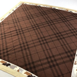 May include: A brown and beige plaid fabric with a white border. The border has a pattern of stylized birds and flowers.