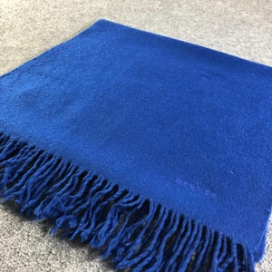 Może przedstawiać: Jasny niebieski szal z frędzlami. Na szalu wyszyte jest słowo "REISS".