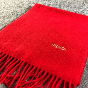 May include: A red wool scarf with fringed edges and the word "FENDI" embroidered in gold.
