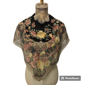 Puede incluir: Un pañuelo de seda negro y marrón con un patrón floral y detalles de paisley. El pañuelo presenta un gran diseño floral con flores amarillas, rosas y blancas. El texto "Anne Klein" es visible en la esquina inferior del pañuelo.
