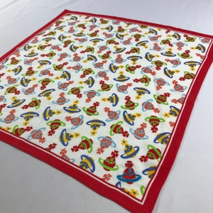 Peut inclure: Un bandana en coton blanc avec une bordure rouge. Le bandana est recouvert d'un motif répété de sphères colorées.