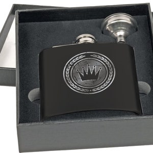 May include: A black flask with a silver crown design inside a laurel wreath, presented in a black gift box. Includes a silver funnel for easy filling. The flask is made of stainless steel and is a great gift.