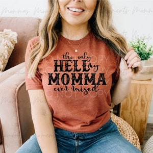 Puede incluir: Una camiseta de color óxido con el texto "the only HELL my MOMMA ever raised" impreso en negro.