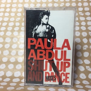 May include: A cassette tape with a red and white design. The tape features a photo of Paula Abdul and the text "Paula Abdul Shut Up And Dance Mixes".