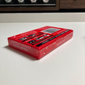 May include: A red Maxell UR 60 audio cassette tape in its original plastic shrink-wrap packaging. The rectangular box features white text, a barcode, and technical specifications including IEC TYPE I EQ 120 &micro;s. The branding Maxell UR 60 is visible.
