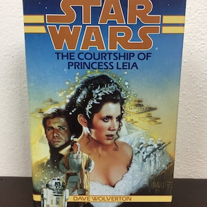 May include: A vintage paperback book titled "Star Wars: The Courtship of Princess Leia" with cover art featuring Princess Leia, Han Solo, and R2-D2. The cover has a blue background with the Star Wars logo in gold.