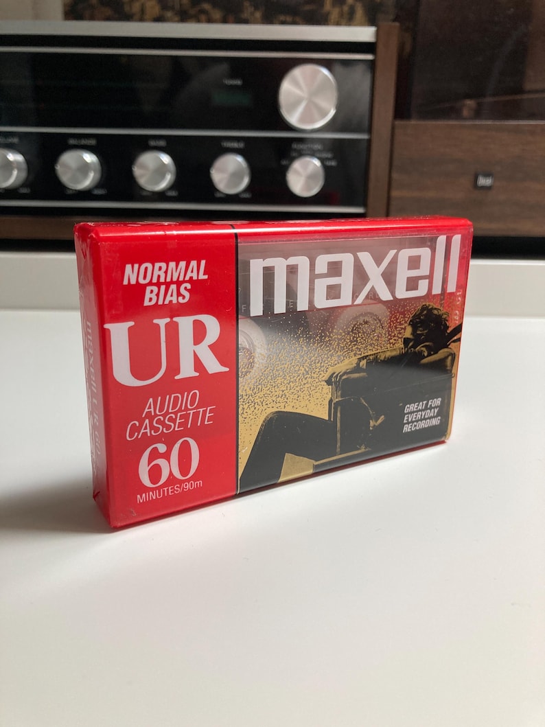 May include: A sealed Maxell UR 60-minute normal bias audio cassette in a red and black plastic case. The packaging features the text Normal Bias, UR, Audio Cassette, 60 Minutes/90m, maxell, and Great For Everyday Recording with a graphic illustration.