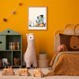 Puede incluir: Una pared amarilla con una ilustraci&oacute;n enmarcada de una deidad elefante azul con una corona y flores. La ilustraci&oacute;n est&aacute; rodeada por un borde blanco y un marco de madera. Un juguete de peluche de llama est&aacute; en primer plano, junto con un estante de madera verde con juguetes y una cama de mimbre marr&oacute;n con un edred&oacute;n estampado en marr&oacute;n y blanco.