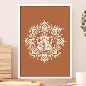May include: A framed art print featuring a cream-colored illustration of the Hindu deity Ganesha within a detailed mandala design. The artwork is set against a warm, earthy brown background, creating a striking contrast. The print is displayed in a white frame.