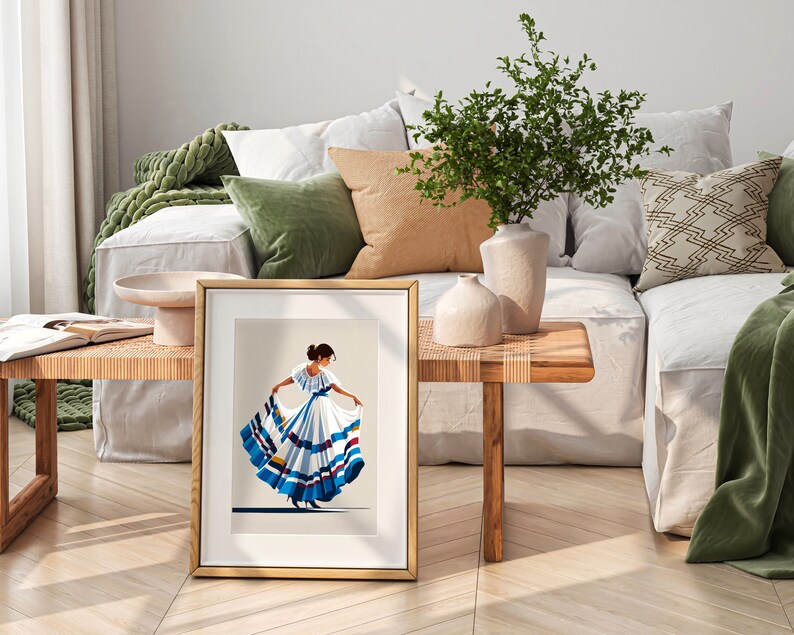 May include: A framed print featuring a stylized illustration of a woman in a traditional white dress with blue and red accents. The artwork is displayed on a wooden table, with a neutral background and a gold frame. The scene is set in a well-lit, modern living space.