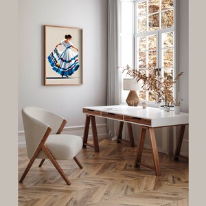 May include: A framed print of a woman in a traditional dress with a full skirt, in shades of white, blue, and brown. The artwork hangs on a neutral-colored wall above a modern desk and chair, creating a stylish interior design.