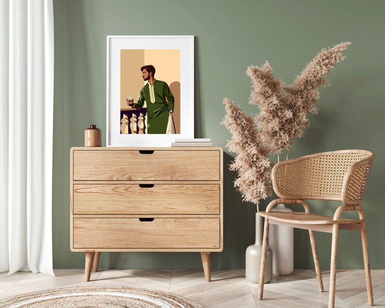 May include: A framed illustration of a man in a green suit standing in front of a balcony with a glass in his hand. The illustration is on a wooden dresser with three drawers. A wicker chair and a dried flower arrangement are in the foreground.