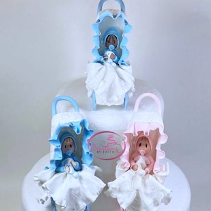 Puede incluir: Tres adornos para pastel de baby shower, cada uno con un bebé en un cochecito. Los cochecitos son azules y rosas, y los bebés llevan vestidos blancos. Los adornos están hechos de fondant y son perfectos para un pastel de baby shower.