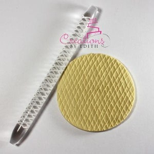 Puede incluir: Un rodillo de acrílico transparente con un patrón de diamante y una impresión de fondant amarillo que muestra el mismo patrón de diamante.