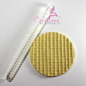 May include: A clear, rectangular rolling pin with a grid pattern and a round, yellow, waffle-textured fondant stamp. The stamp is approximately 3 inches in diameter. The image includes the text "Creations by Edith".