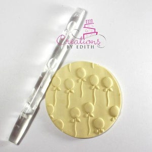 Peut inclure: Un rouleau à pâtisserie en acrylique transparent avec un motif de ballons en relief sur la surface. Le rouleau à pâtisserie est utilisé pour créer des motifs décoratifs sur le fondant ou la pâte.