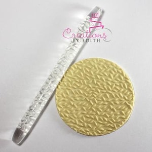 May include: A clear acrylic rolling pin with a textured leaf pattern and a matching circular pale yellow fondant disc featuring the same embossed leaf design. The rolling pin is marked with the logo Creations by Edith in pink and black text.