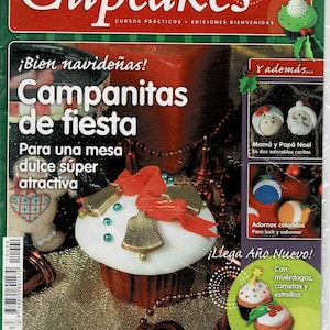 May include: A magazine cover featuring a cupcake decorated with red ribbon, gold bells, and green and gold beads. The magazine is titled "Cupcakes" and the cover text reads "¡Bien navideñas! Campanitas de fiesta Para una mesa dulce súper atractiva" and "Y además... Mamá y Papá Noel En dos adorables caritas" and "Adornos coloridos Para lucir y saborear" and "¡Llega Año Nuevo! Con muérdagos, cometas y estrellas" and "BIEN venidas".