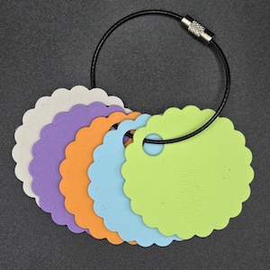 May include: A set of five circular tags with scalloped edges in white, purple, orange, light blue, and lime green. Each tag features a single circular hole near the top edge, and all are held together by a thin black metal cable ring.
