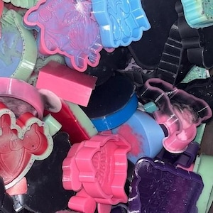 Könnte beinhalten: Eine Auswahl an bunten Seifenformen in verschiedenen Formen und Farben. Die Formen sind in den Farbtönen Rosa, Blau, Grün und Schwarz gehalten. Einige Formen haben Glitzerakzente. Das Bild ist eine Nahaufnahme der Formen.
