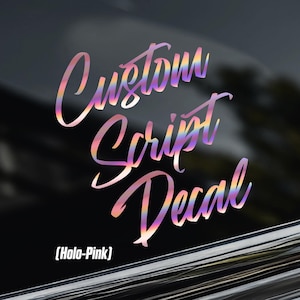 Peut inclure: Un autocollant holographique rose en écriture cursive appliqué sur une vitre de voiture sombre. Le texte indique Custom Script Decal. Un petit logo avec les lettres CA surmontées d'une couronne est visible dans le coin supérieur gauche.