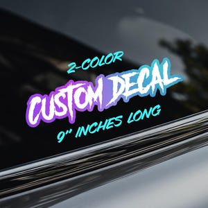 May include: A 2-colour custom decal measuring 9 inches long, featuring the text 2-COLOR CUSTOM DECAL 9 INCHES LONG in a stylised font. The lettering displays a gradient of purple and light blue colours, applied to a dark tinted glass surface.