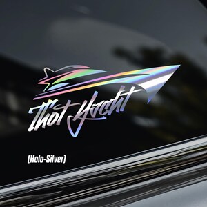 May include: Holographic silver car decal featuring a stylized yacht design with the text "Thot Yacht" in a script font. The decal has a rainbow sheen and the text "(Holo-Silver)" is below the yacht.