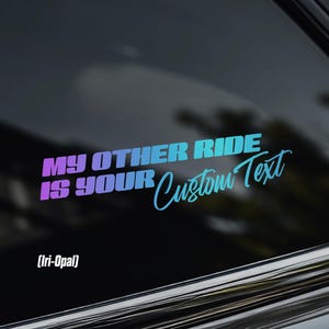May include: A vinyl decal applied to a car window featuring the text MY OTHER RIDE IS YOUR Custom Text in a gradient colour scheme transitioning from purple to blue. The decal includes the text Iri-Opal in the lower left corner of the design.